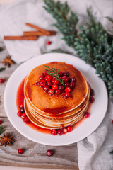 Stack of american pancakes with fresh cranberry and jam in white plate on wooden rustic table decorated Christmas tree, delicious dessert for breakfast in winter, vintage style. 