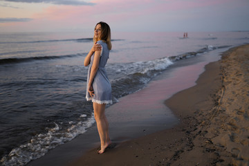 Standing full height: Portrait of a Beautiful blonde woman in a light blue dress on the Baltic Sea beach during sunset with vivid colors © dissx
