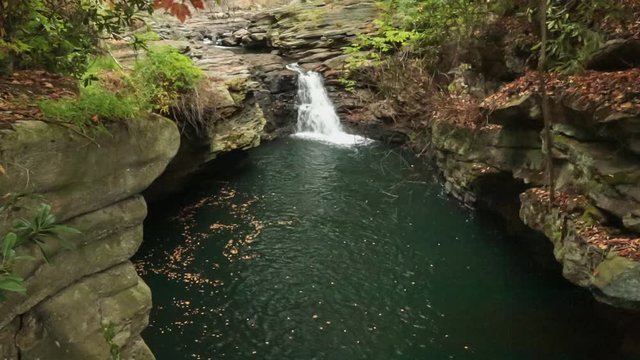 A waterfall pours into a pool on the Roaring Brook river in Pennsylvania while autumn leaves drift down in the breeze.