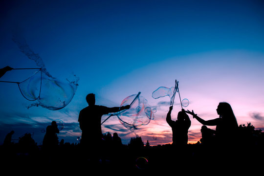 Silhouettes of people blowing bubbles at dusk