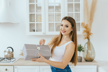 Beautiful young woman holds New Year present in modern bright Scandinavian kitchen