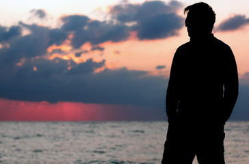 Fototapeta premium A black silhouette of a man standing at a beach and observing in front of the ocean sunrise or sunset. A place for text