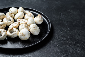 Raw mushrooms champignon on a plate. Black background. Top view. Space for text