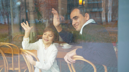 Fototapeta na wymiar Father and son waves to someone through the window in cafe