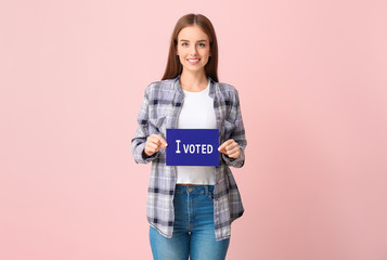 Naklejka premium Young woman holding paper with text I VOTED on color background