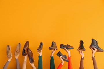 Many hands with different stylish shoes on color background