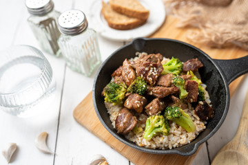 Beef and broccoli over rice in a black skillet topped with sesame seeds 