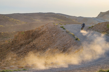 A professional motorcycle rider on a desert dirt track. Dirt and dust rise from the wheels. © MagioreStockStudio