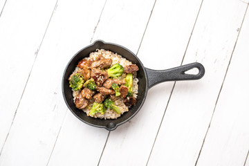 Beef and broccoli over rice in a black skillet topped with sesame seeds 