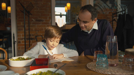 Father and son in a cafe, boy writes in notebook