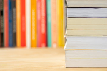 Pile of books in fronto of unfocused books over a wooden table