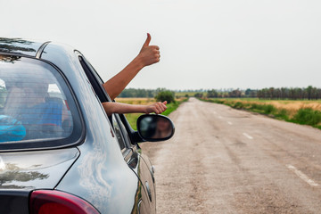 Happy traveler with thumbs up. People on the road concept. Woman showing thumbs up from car window with sunset sky at background