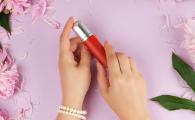 female hands with smooth fair skin keep liquid red lipstick in a tube