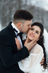 Beautiful wedding of amazing couple. Young couple in love, groom and bride in wedding dress at the nature. Wedding. Wedding day. Bride and groom hugging in the snowy forest at their fairy wedding day
