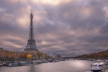 Fototapeta na wymiar Paris, France - November 24, 2019: The Eiffel tower from embankment at the river Seine in Paris. Ship and boats on river at cloudy day