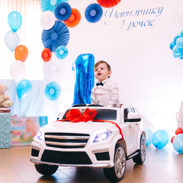 baby boy sits in electric car near photo zone with paper decor a