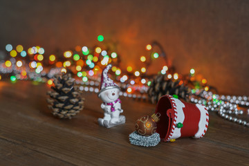 New Year's card - a bucket with gifts on a wooden background, a multi-colored garland and a snowman figurine. New Year and Christmas gifts.