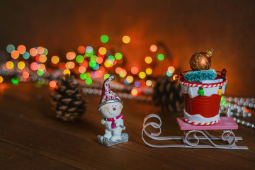 Small snowman toy with wooden sleigh and gift bucket on lights background - New Year 2020, Christmas