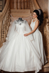 Fototapeta premium Wedding details. A special day. The bride touches the wedding dress on the mannequin. Bride with luxury delight make-up and hairstyle. Stylish bride getting ready in the morning in the room