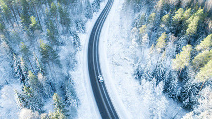 White car drives empty road in forest in the cold Finnish winter. Tourists on road trip cruising through the idyllic snow covered countryside and woods. - 307497466