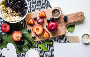 Creative layout  of a healthy breakfast. A composition of fresh summer fruits, muesli, grains, plums on a cutting board and tablecloth. Healthy food. Top view with space for text.