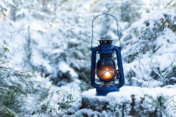  Lantern standing and glowing in the snow at evening. Vintage hand lantern a wooden stump in the...