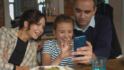 Parents and daughter look at phone and laughs at photographs 
