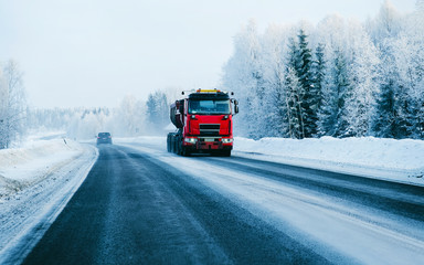 Fototapeta na wymiar Winter road with snow. Truck in Finland. Lorry car and cold landscape of Lapland. Europe forest. Finnish City highway ride. Roadway and route snowy street trip. Delivery in downhill driveway driving