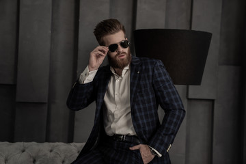 Handsome stylish man in blue suit in a cage at home sitting on sofa