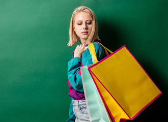 Blonde girl in 90s style jacket with shopping bags on green background