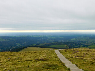 Paysage d'Auvergne au sommet bien vert et petit chemin de bois avec large vue panoramique et ciel nuageux