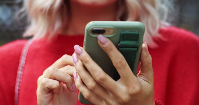 Close up view of fashionable girl hands using modern smartphone outside on the street looking for new beauty salon in this area. Internet searching. Traveling blonde woman using device at first