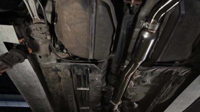 Moving crane shot showing the undercarriage chasis of vehicle lifted at the car service garage