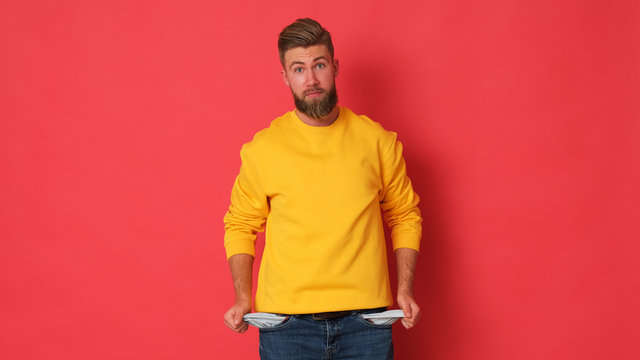 Young man is showing his pocket out. Man in yellow blouse on red background. Empty pockets. 