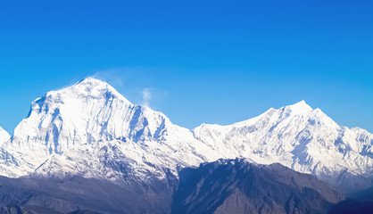 Mountain landscape panorama. Majestic mountain peaks covered with snow against a bright blue sky.