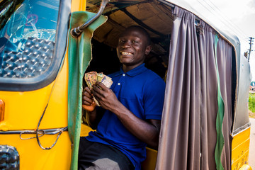 young african man driving a rickshaw taxi counting his money smiling