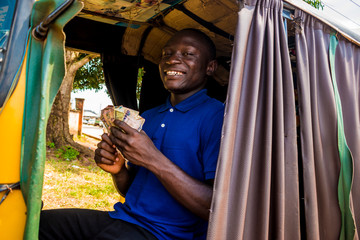 young african man driving a rickshaw taxi counting his money smiling