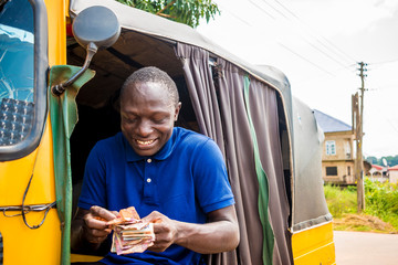 young african man driving a rickshaw taxi counting his money smiling