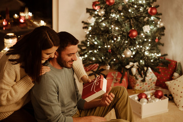 woman giving gift box to man; indoor photo with xmas decoration on background
