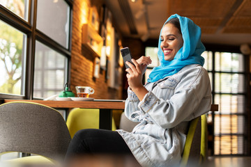 Young woman wearing turquoise hijab and using smartphone in a cafe