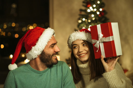 smiling woman giving gift box to man; photo with xmas decoration on background; christmas celebraiting concept