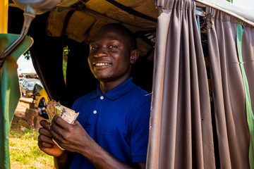 Obraz na płótnie Canvas young african man driving a rickshaw taxi counting his money smiling