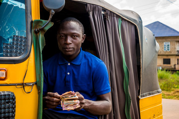 young african man driving a rickshaw taxi counting his money smiling