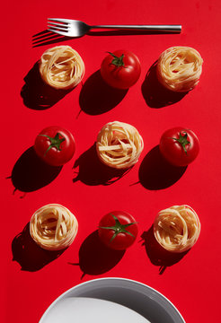 Directly above shot of pasta with tomatoes arranged by fork on red background