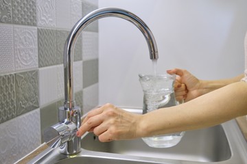 Woman pouring water into jug from kitchen faucet