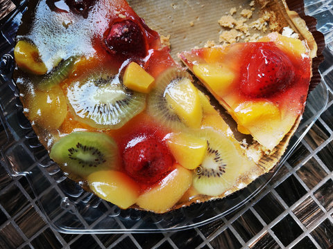 Round fruit cake with assorted jelly fruits, strawberries, peach and kiwi slices on a tiled surface. Healthy food. Flat lay close-up photo of cut pieces of vegetarian dessert on shiny mosaic table.