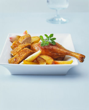 Close-up of Roasted duck leg with apples and potatoes in plate on table