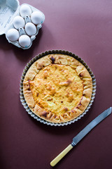 Quiche with.egg, cream, scamorza cheese and spec ham, round shaped on an aluminium mold, top view on a dark brown background