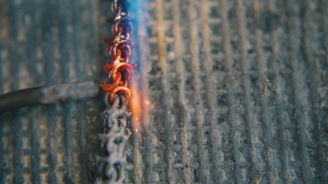 CU shot: welding of gold metal chain links with jeweler needle and gas burner on fireproof asbestos sheet closeup