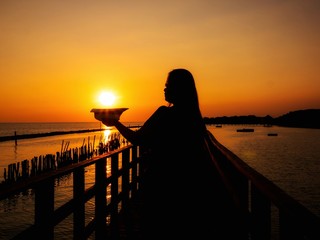 A woman silhouette standing Selfie on wooden pier at the sea with beautiful cloudy sunset.